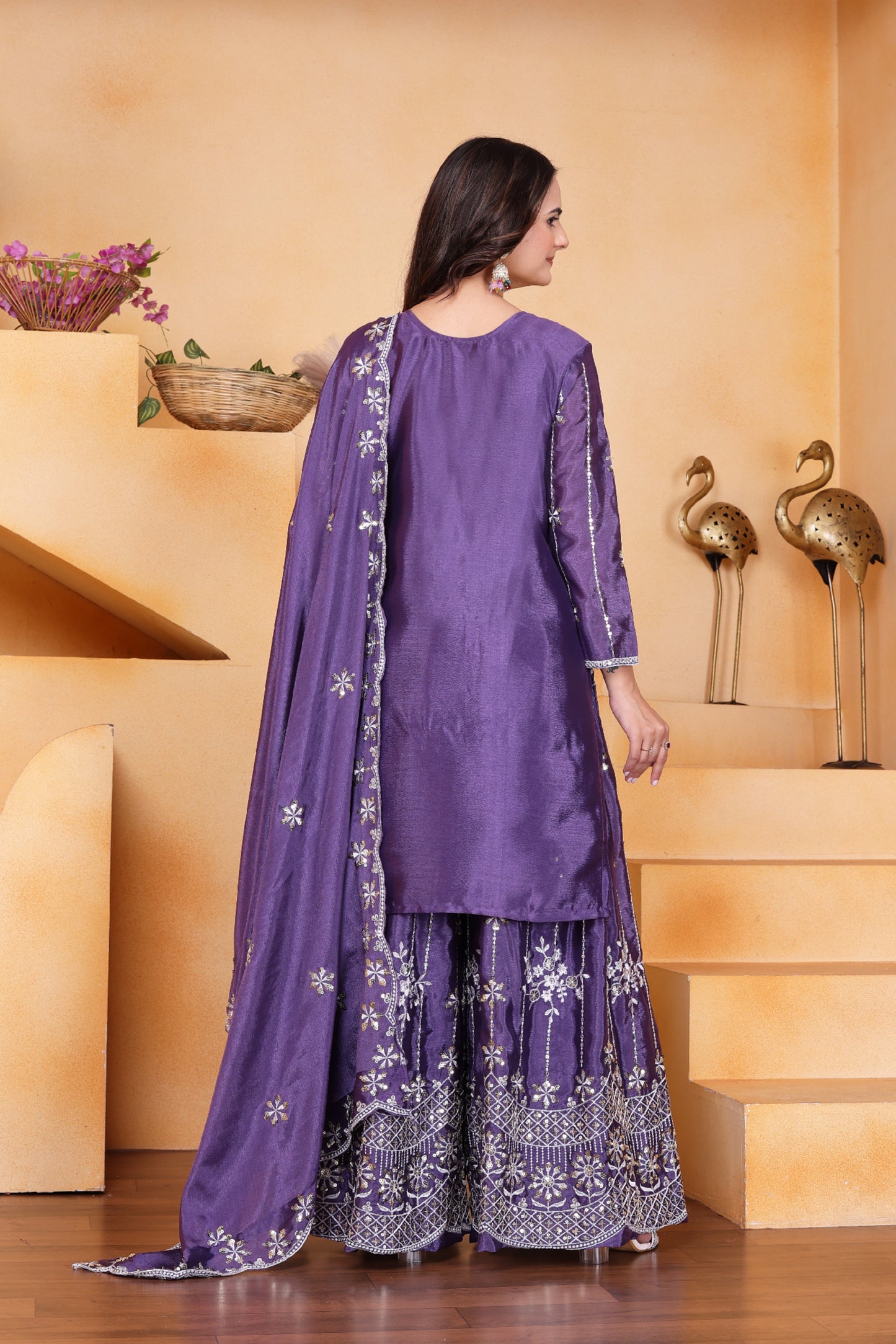Woman wearing a purple traditional outfit with floral patterns in a decorative setting.