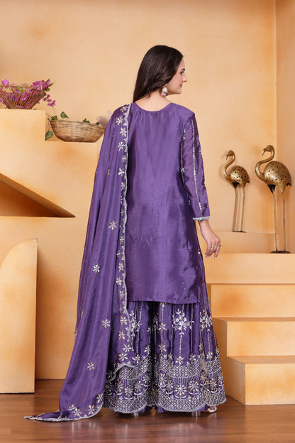 Woman wearing a purple traditional outfit with floral patterns in a decorative setting.